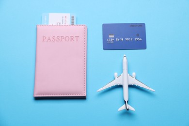 Photo of Airplane model, flight ticket, passport and credit card on light blue background, flat lay