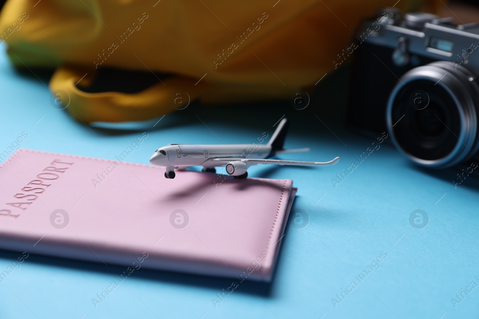 Photo of Airplane model, passport, vintage photo camera and backpack on light blue background, closeup