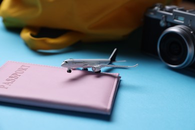Photo of Airplane model, passport, vintage photo camera and backpack on light blue background, closeup