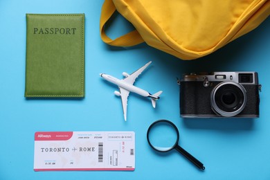 Photo of Airplane model, passport, flight ticket, magnifying glass, vintage photo camera and backpack on light blue background, flat lay