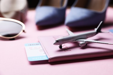 Photo of Airplane model, passport, flight ticket and shoes on pink background, closeup