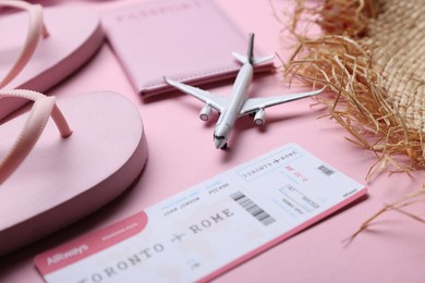 Photo of Airplane model, passport, flight ticket, flip flops and straw hat on pink background, closeup