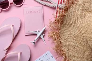 Photo of Airplane model, passport, flight ticket and accessories on pink background, flat lay