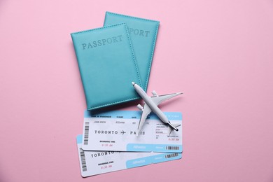 Photo of Airplane model, flight tickets and passports on pink background, flat lay