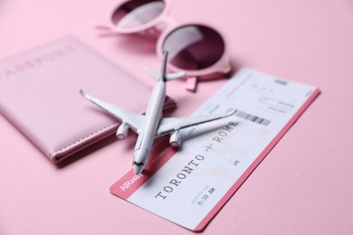 Photo of Airplane model, flight ticket, passport and sunglasses on pink background, closeup