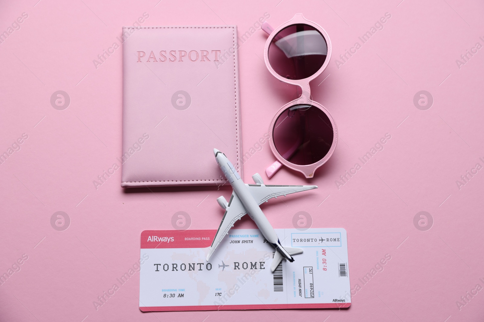 Photo of Airplane model, flight ticket, passport and sunglasses on pink background, flat lay