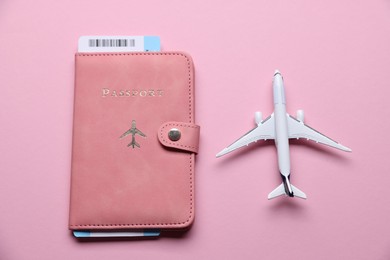 Photo of Airplane model, flight ticket and passport on pink background, flat lay