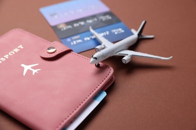 Photo of Airplane model, flight ticket, passport and credit cards on brown background, closeup