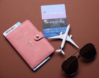 Photo of Airplane model, flight ticket, passport, credit cards and sunglasses on brown background, flat lay