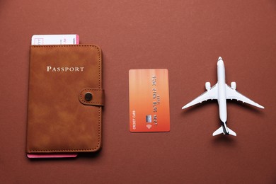 Photo of Airplane model, flight ticket, passport and credit card on brown background, flat lay
