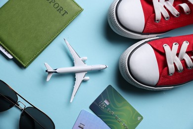 Photo of Airplane model, passport, credit cards, sunglasses and sneakers on light blue background, flat lay