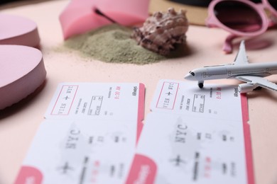Photo of Flight tickets, airplane model, sand and beach accessories on beige background, closeup