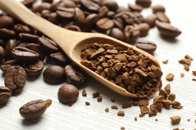 Photo of Spoon with granulated instant coffee and beans on white wooden table, closeup