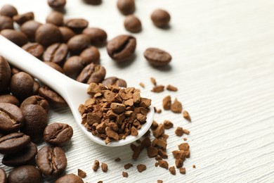 Photo of Spoon with granulated instant coffee and beans on white wooden table, closeup