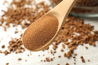 Photo of Spoon with instant coffee powder above white wooden table, closeup