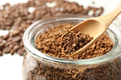 Photo of Spoon with granulated instant coffee and jar on white table, closeup