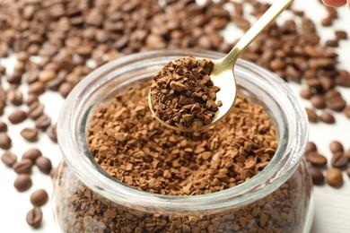 Photo of Spoon with granulated instant coffee and jar on white table, closeup