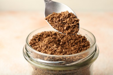 Photo of Taking granulated instant coffee from jar with spoon on blurred light background, closeup