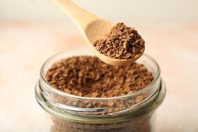 Photo of Taking granulated instant coffee from jar with spoon on blurred light background, closeup