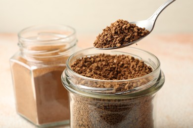 Photo of Spoon with granulated instant coffee and jars on light table, closeup