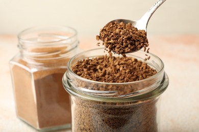 Photo of Taking granulated instant coffee from jar with spoon at light table, closeup
