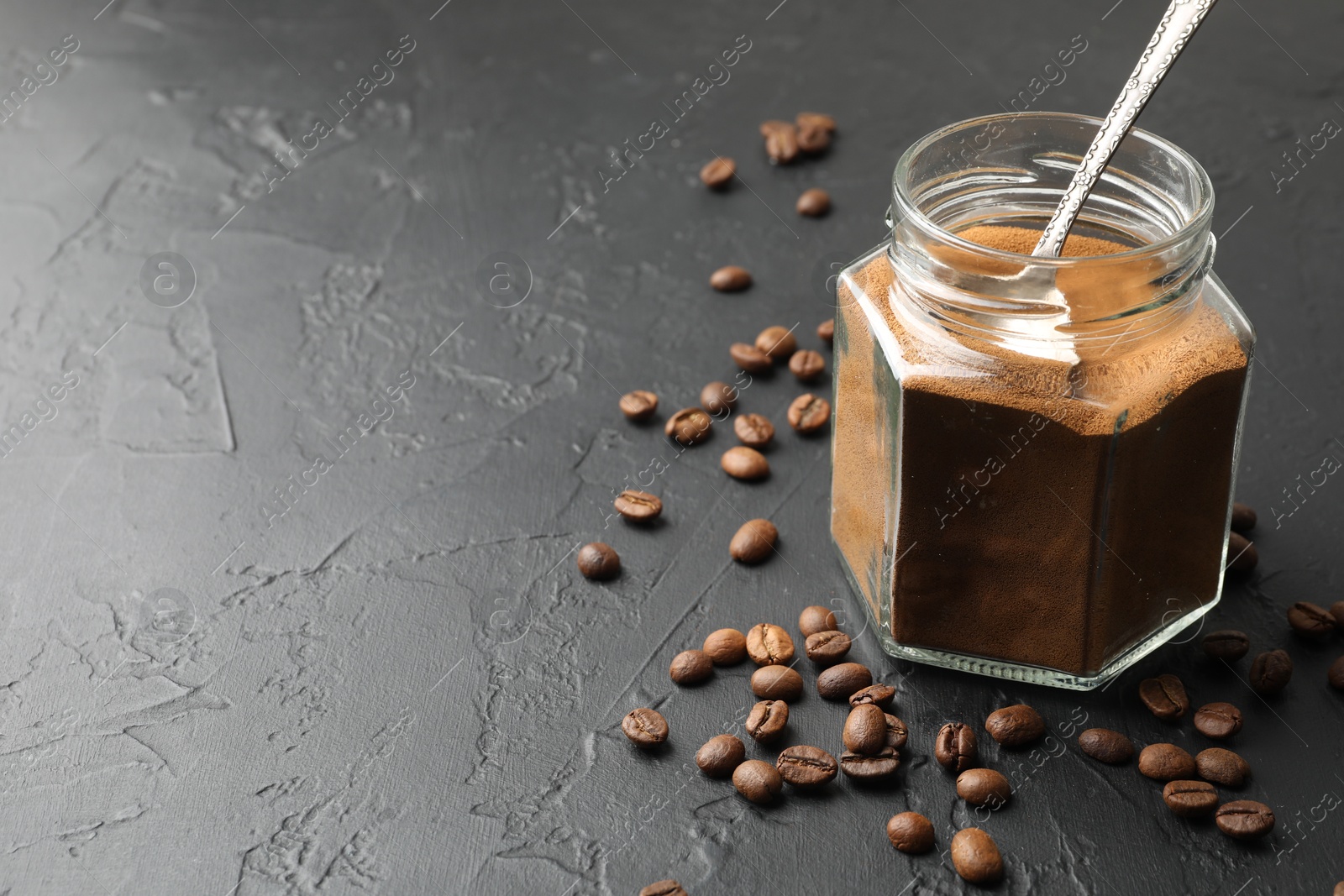 Photo of Instant coffee powder in jar and beans on dark textured table, closeup. Space for text