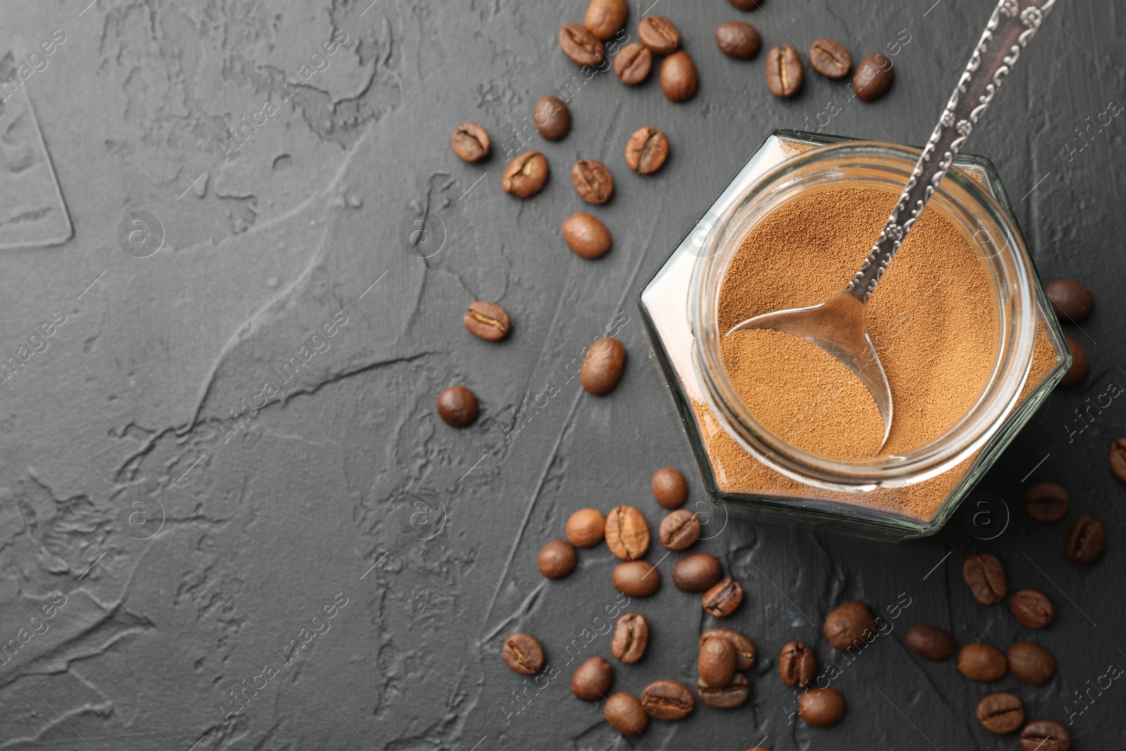 Photo of Instant coffee powder in jar and beans on dark textured table, flat lay. Space for text