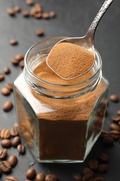 Photo of Taking instant coffee powder from jar with spoon at dark table, closeup