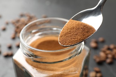 Photo of Spoon with instant coffee powder and jar on dark table, closeup