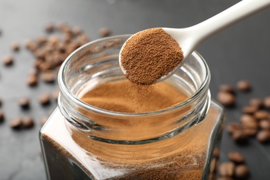 Photo of Adding instant coffee powder from spoon into jar on dark table, closeup
