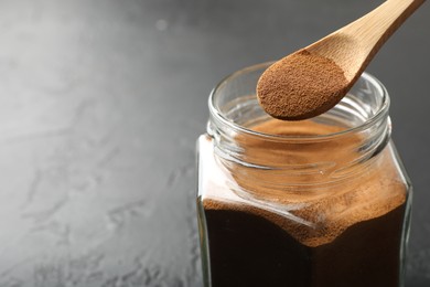 Photo of Adding instant coffee powder from spoon into jar on dark textured table, closeup. Space for text