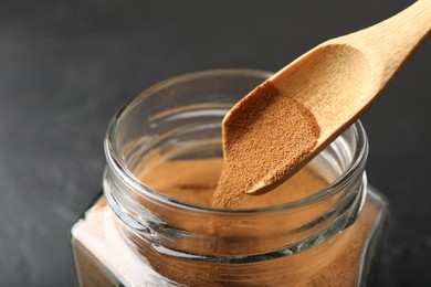 Photo of Adding instant coffee powder from spoon into jar on dark table, closeup