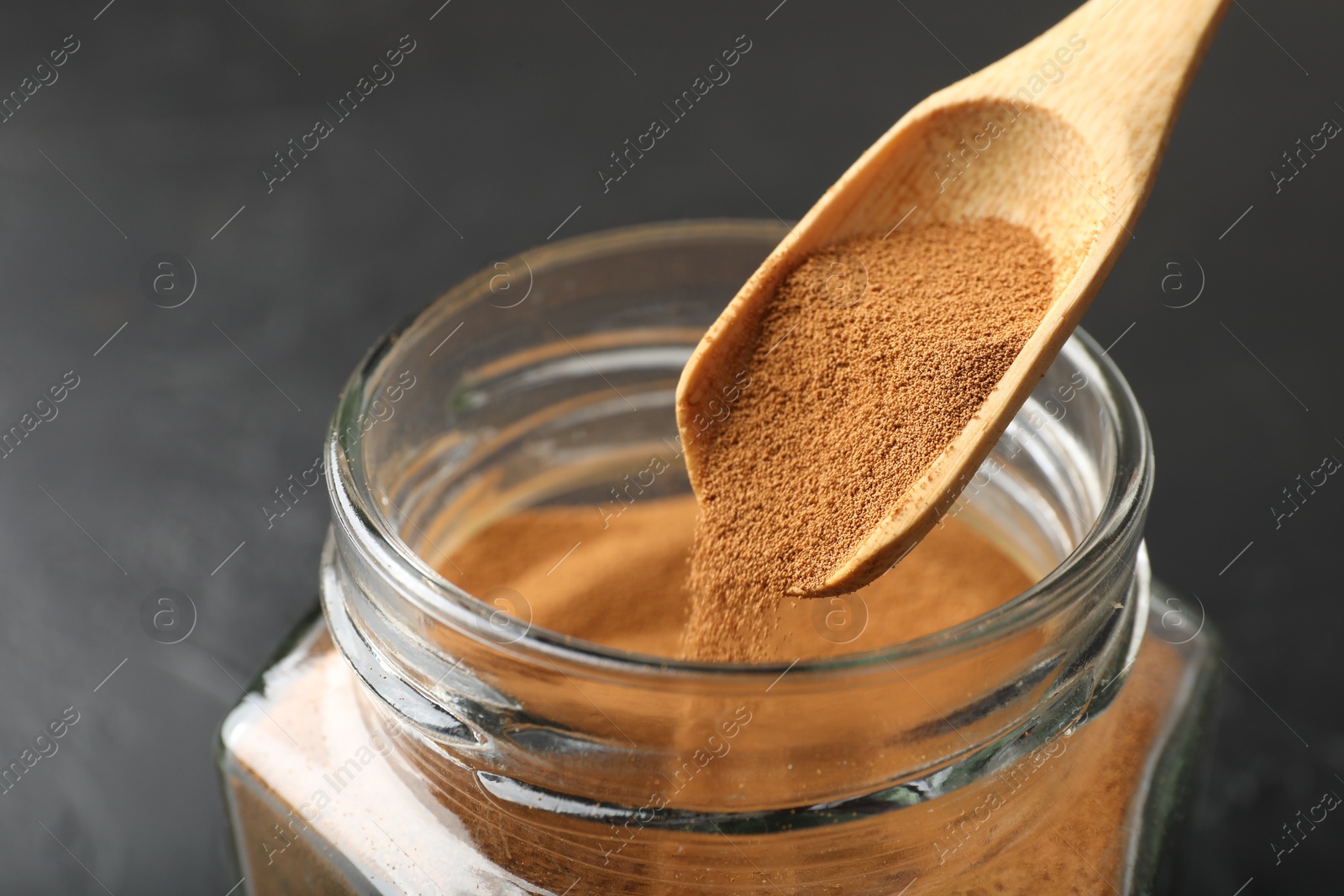 Photo of Adding instant coffee powder from spoon into jar on dark table, closeup