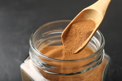 Photo of Adding instant coffee powder from spoon into jar on dark table, closeup