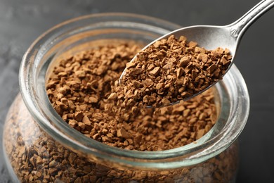 Photo of Adding granulated instant coffee from spoon into jar on dark table, closeup