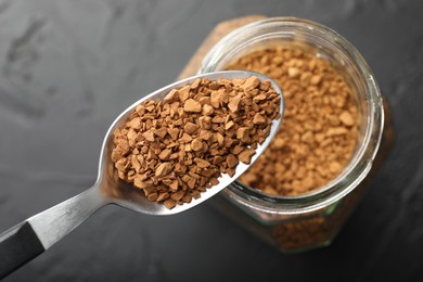 Photo of Spoon with granulated instant coffee and jar on dark textured table, top view