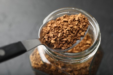 Photo of Spoon with granulated instant coffee and jar on dark table, closeup