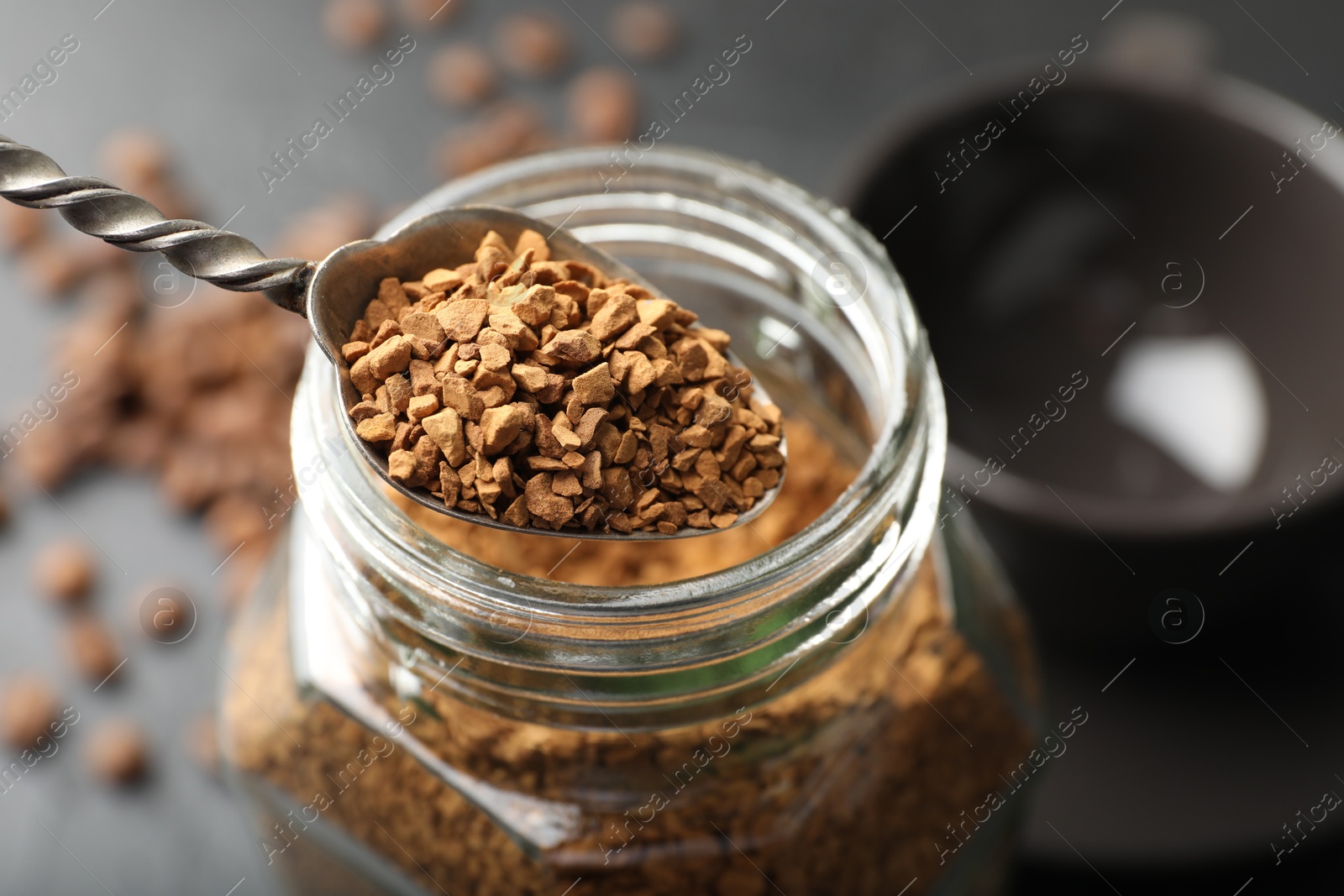 Photo of Spoon with granulated instant coffee and jar on dark table, closeup
