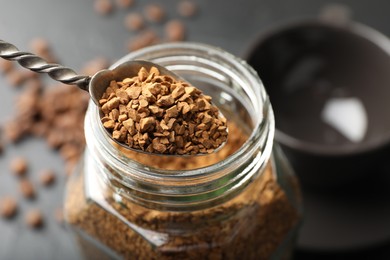 Photo of Spoon with granulated instant coffee and jar on dark table, closeup