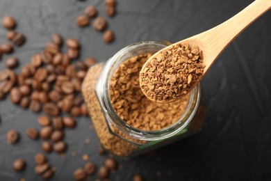 Photo of Spoon with granulated instant coffee, jar and beans on dark textured table, top view