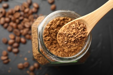 Photo of Spoon with granulated instant coffee, jar and beans on dark table, top view