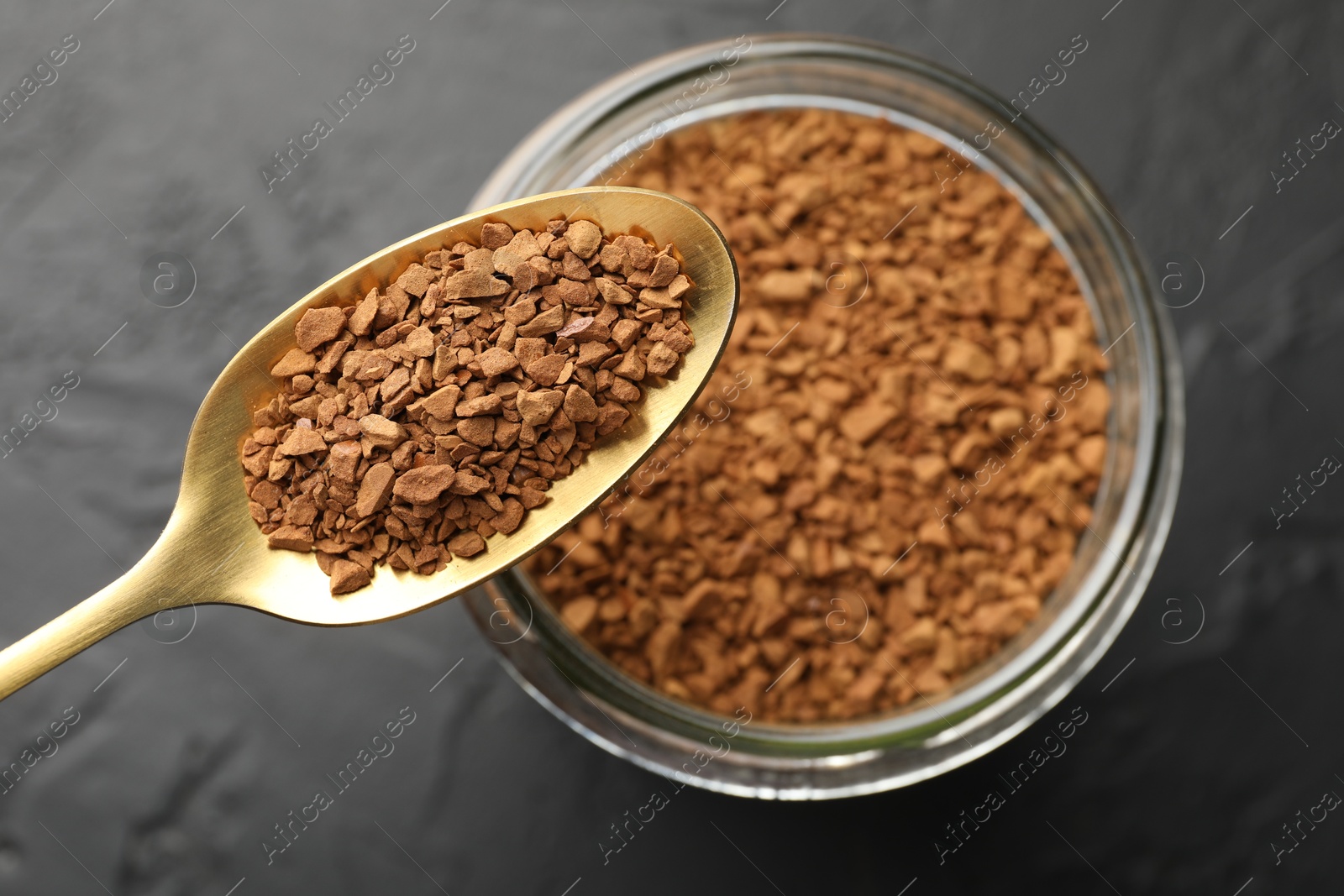 Photo of Spoon with granulated instant coffee and jar on dark textured table, top view