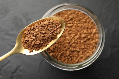 Photo of Spoon with granulated instant coffee and jar on dark textured table, top view