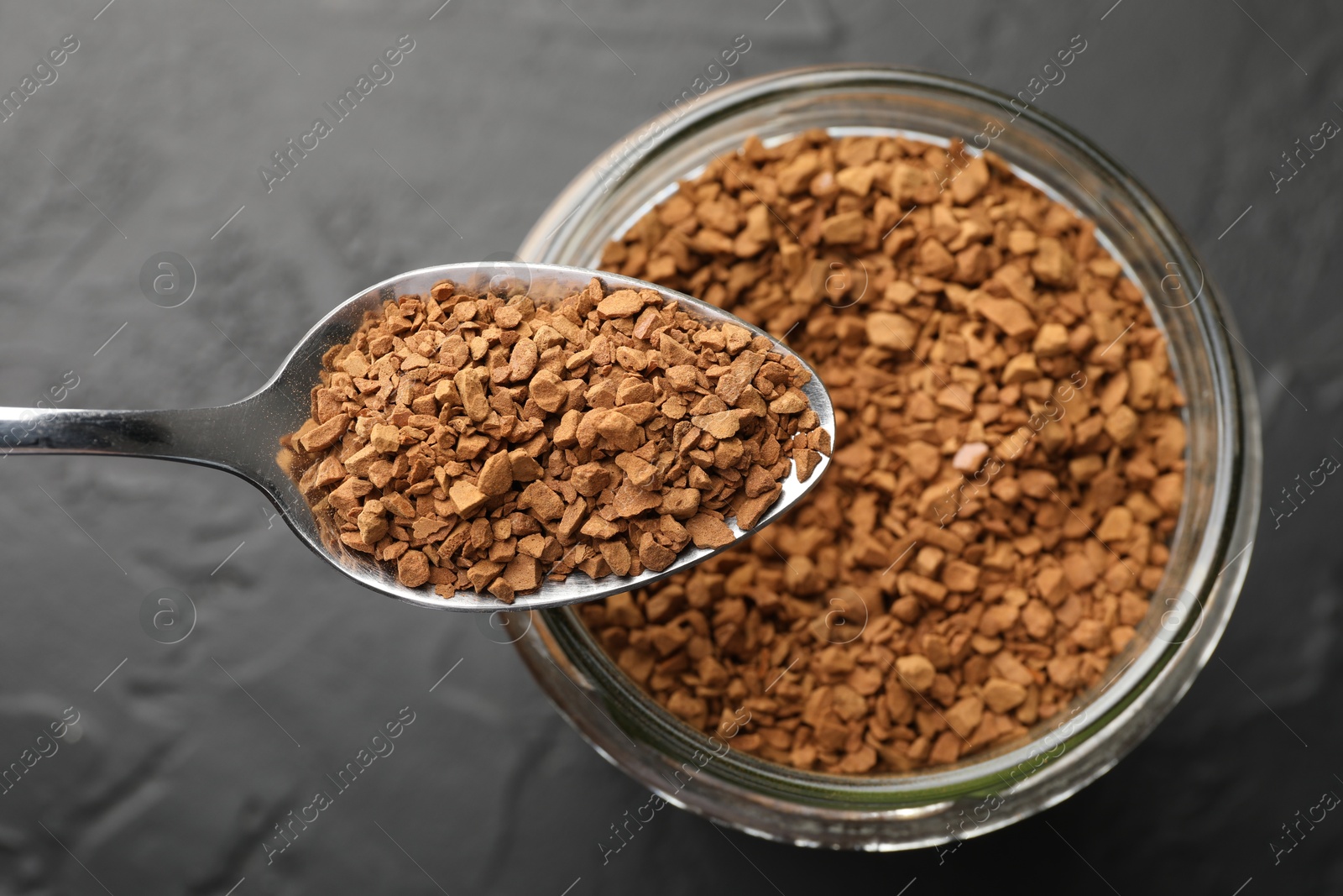 Photo of Spoon with granulated instant coffee and jar on dark textured table, top view