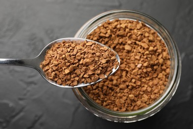Photo of Spoon with granulated instant coffee and jar on dark textured table, top view