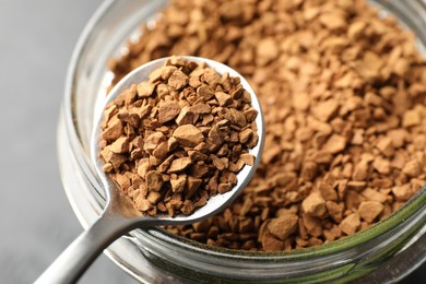 Photo of Spoon with granulated instant coffee and jar on grey background, closeup
