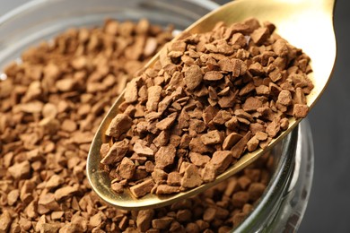 Photo of Adding granulated instant coffee from spoon into jar on grey background, closeup