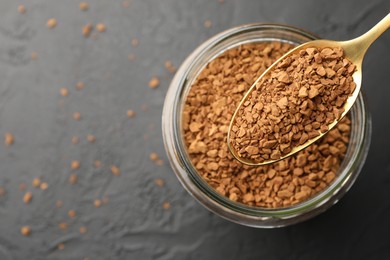 Photo of Spoon with granulated instant coffee and jar on dark textured table, top view. Space for text