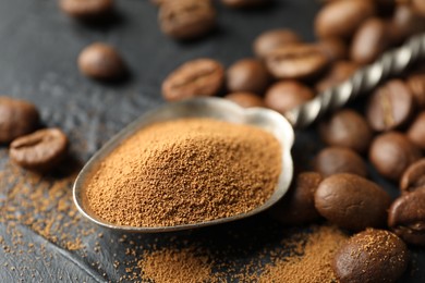 Photo of Spoon with instant coffee powder and beans on dark textured table, closeup