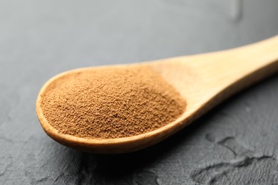 Photo of Spoon with instant coffee powder on dark textured table, closeup